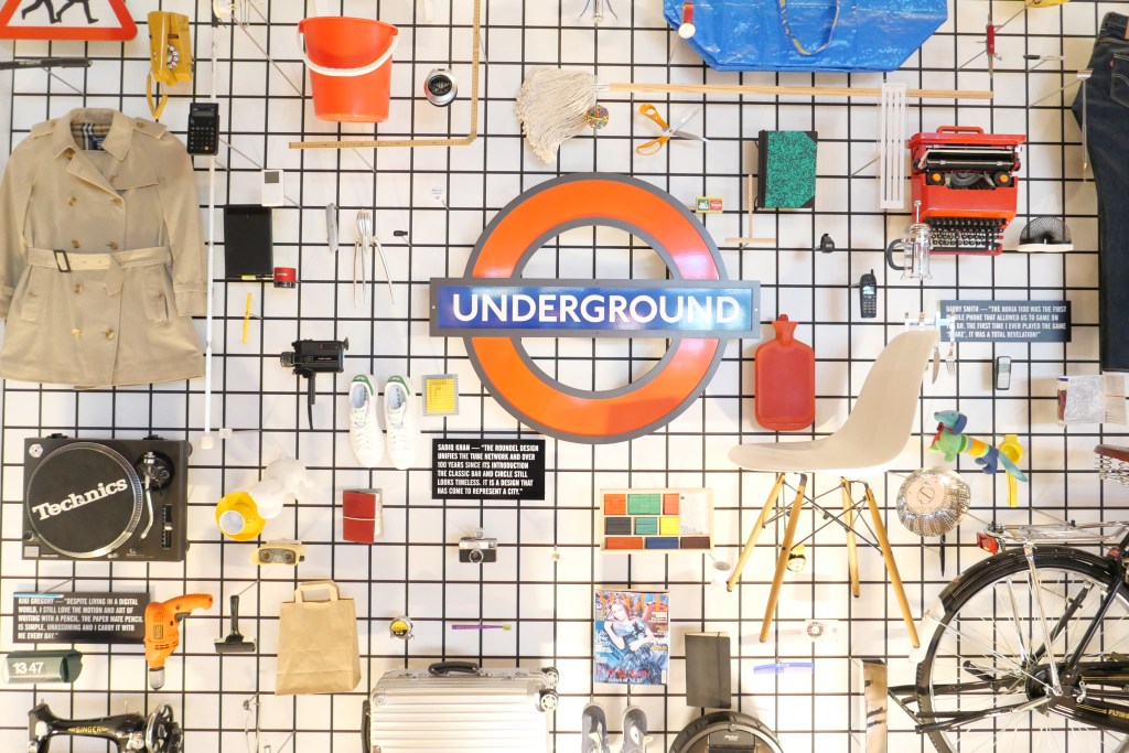 壁に取り付けられた様々なアイテム、中央にロンドン地下鉄のサインがあるデザイン。コート、カメラ、家具、文房具などが配置されている。