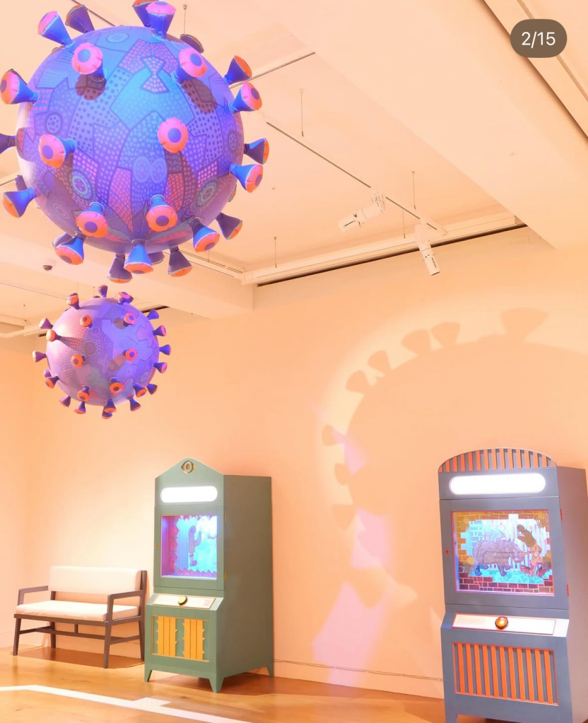 色とりどりのデザインの巨大な球体が天井から吊るされている、近くに二台のインタラクティブなディスプレイがあるアート展示の内部