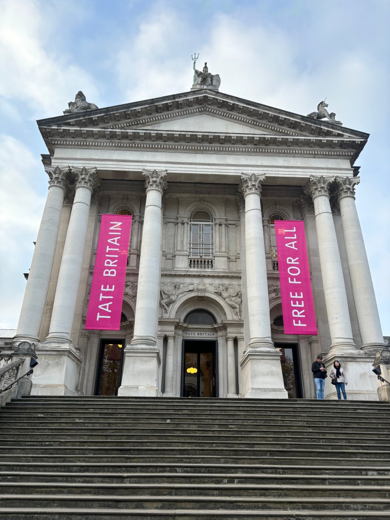 テート・ブリテンの建物の正面、ピンクの看板が掲げられた階段と2人の訪問者